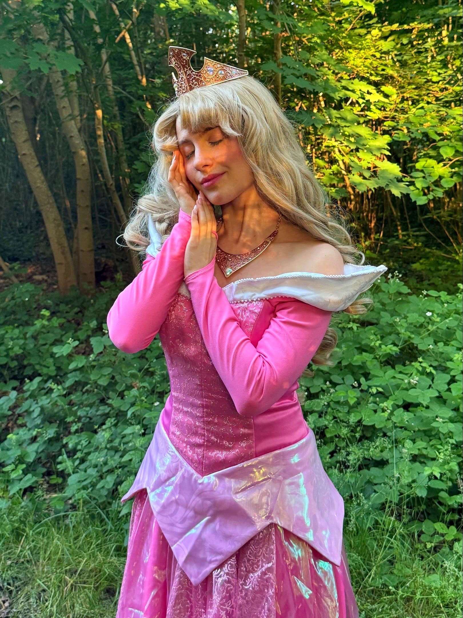 Animatrice costumée en princesse Aurore, les yeux fermés, dans une forêt verdoyante
