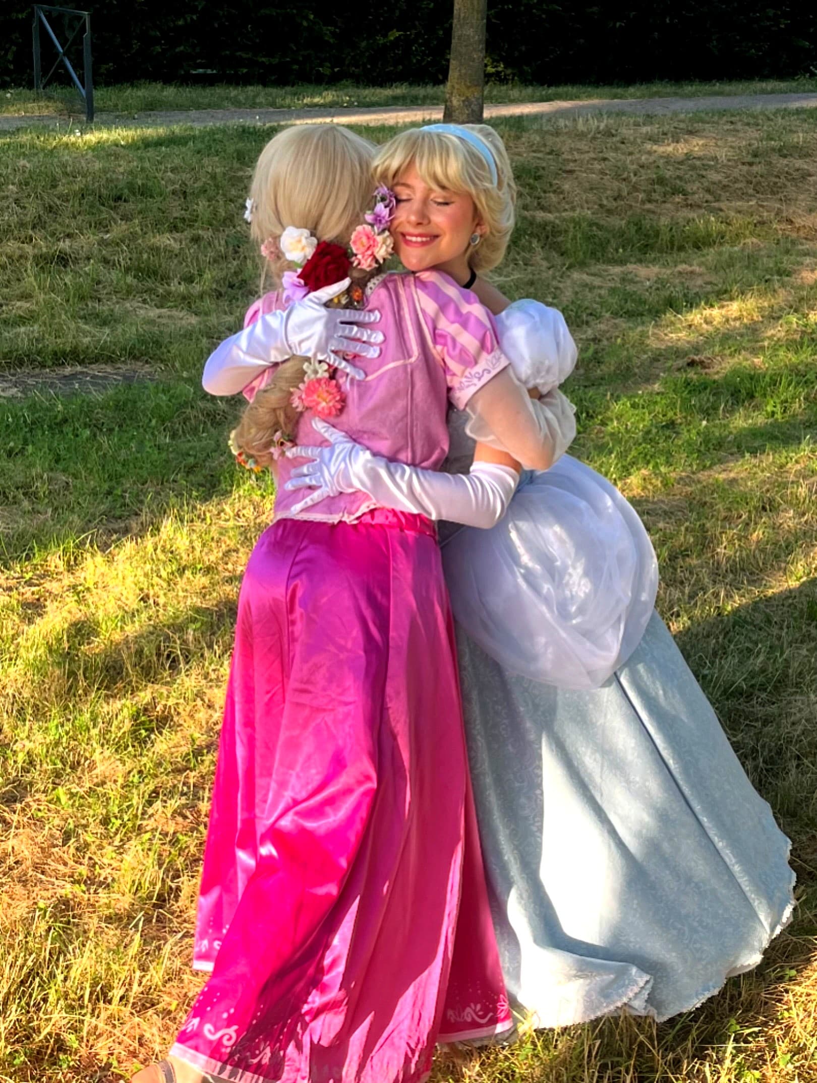 Animatrices costumées en Raiponce et Cendrillon se faisant un câlin complice dans un parc