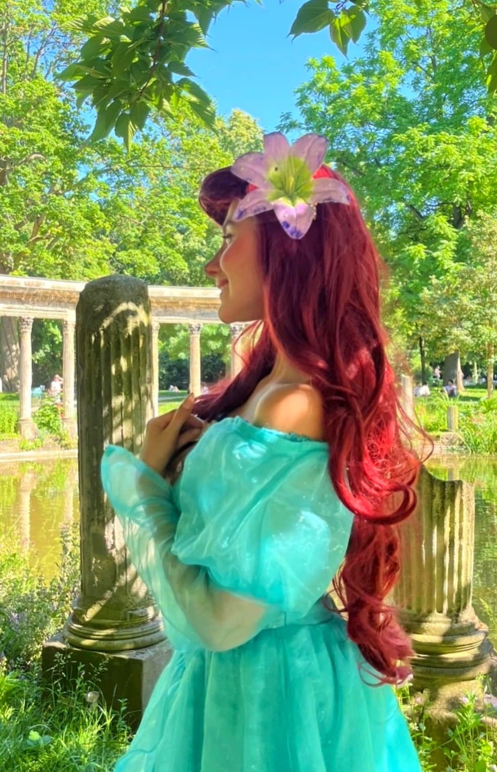 Robe Ariel — Animatrice déguisée en Ariel (La Petite Sirène), longue chevelure rouge et robe turquoise, devant des colonnes antiques au bord d'un bassin, lors d'une animation d'anniversaire Ma Vie de Rêves