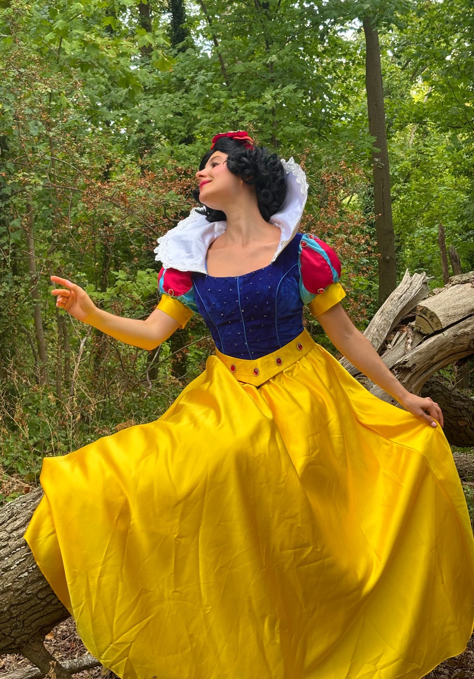 Robe Blanche-Neige — Animatrice déguisée en Blanche-Neige, corset bleu, manches rouges et grande jupe jaune, posant près d'un tronc d'arbre dans une forêt, lors d'une animation d'anniversaire Ma Vie de Rêves