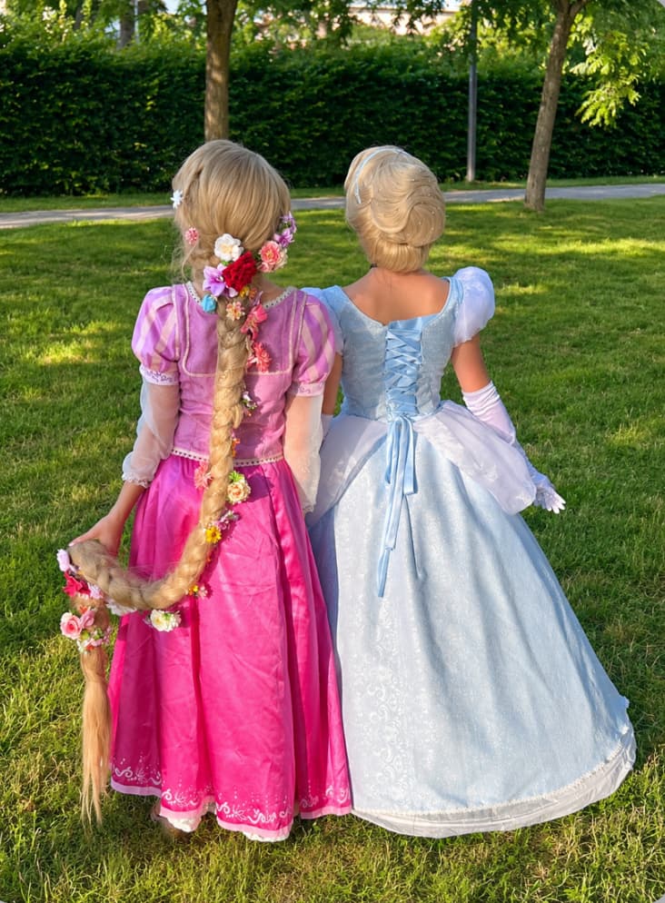 Deux animatrices déguisées en Raiponce et Cendrillon, vues de dos, se tenant par la main dans un jardin, lors d'une animation d'anniversaire Ma Vie de Rêves